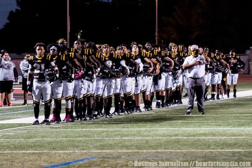 Varsity football players and coach stand together as they honor the flag.